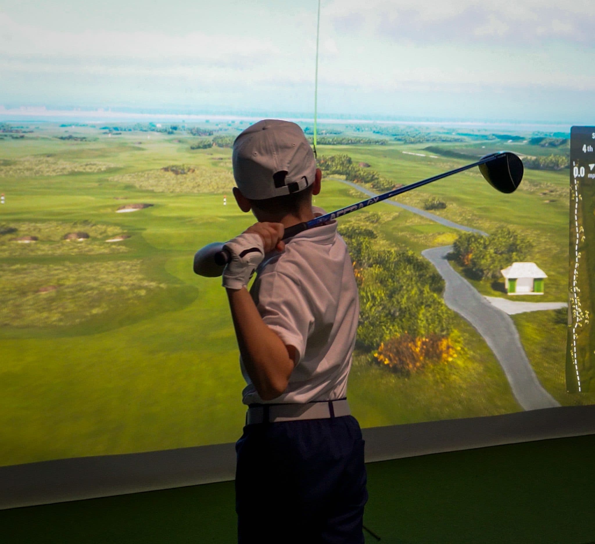 A junior golfer mid-swing in front of the simulator screen
