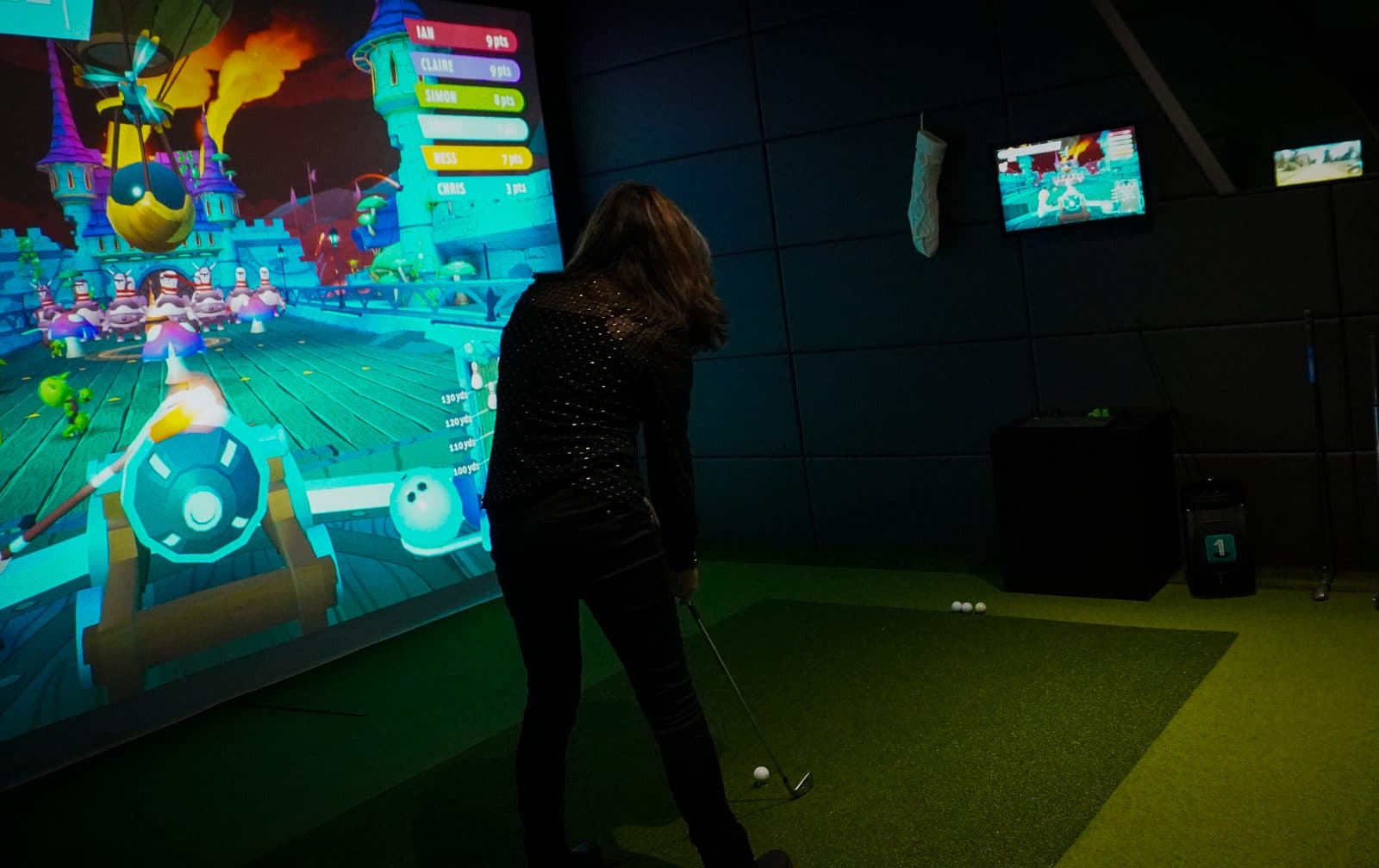 A player teeing off on a colourful party game in a simulator bay