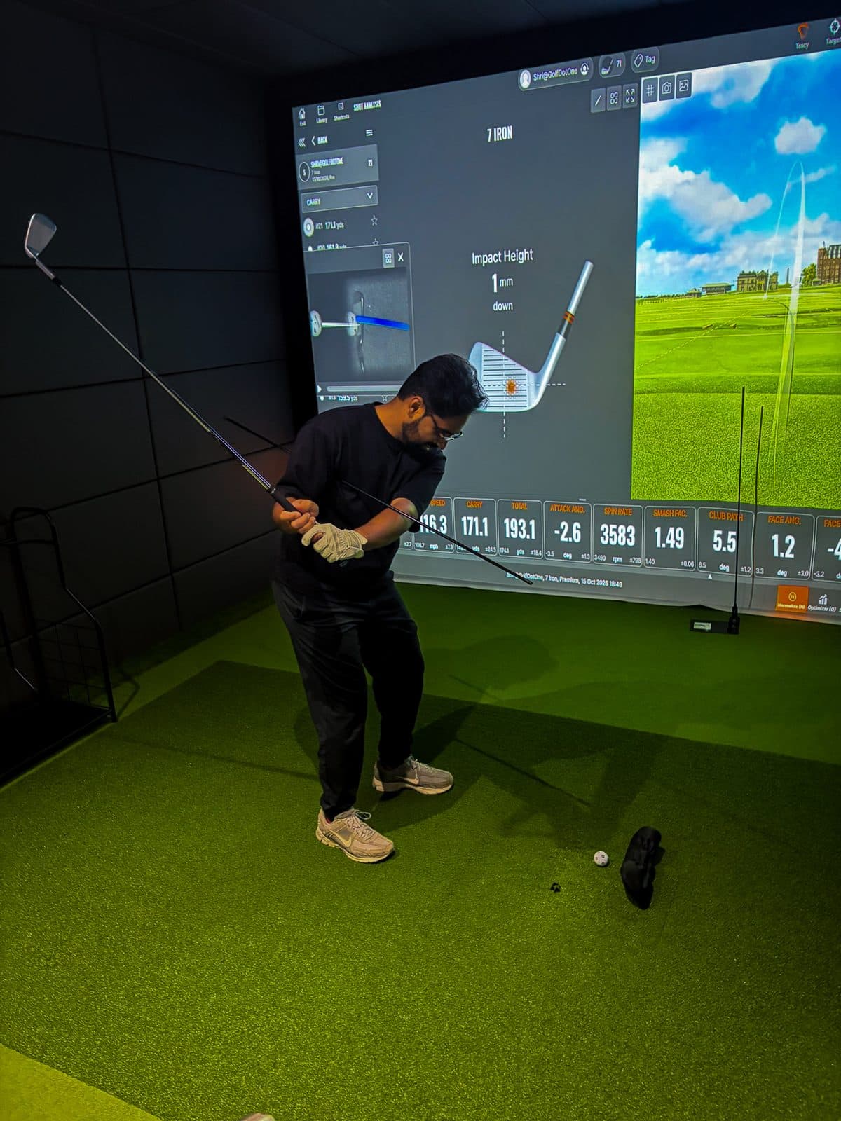 A golfer mid-swing in a Trackman bay with shot data on screen